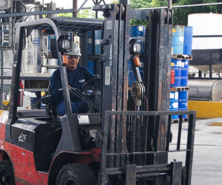 Warehouse scene with worker operating a forklift among blue barrels.